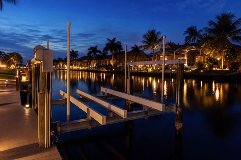 A finished aluminum boat lift and composite dock on a Southwest Florida canal at dusk, with the lift cradle raised above the water