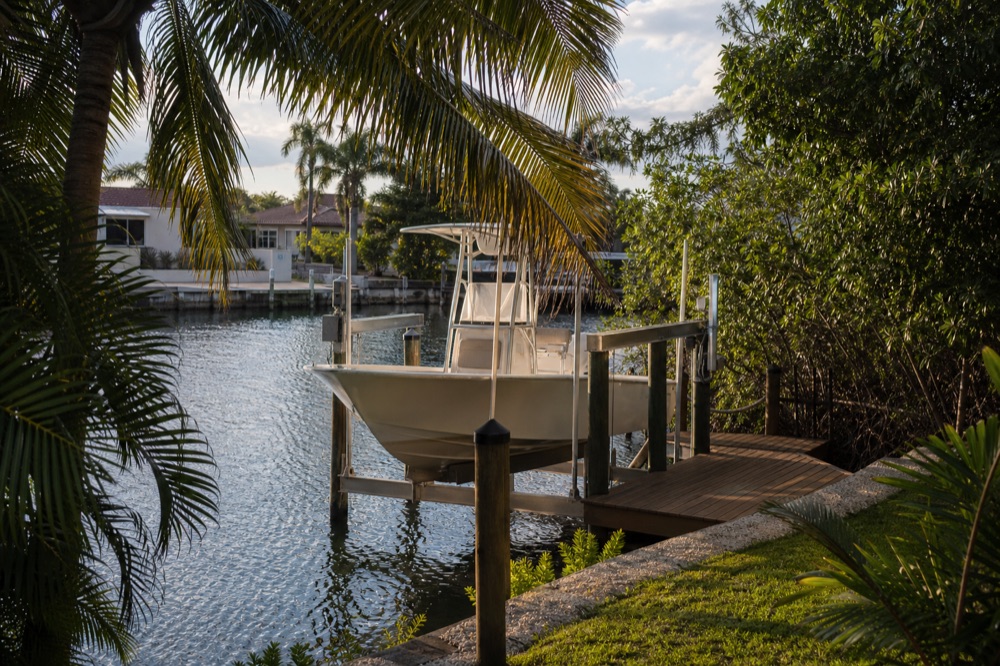 A center console raised on a boat lift beside a wood dock on a Southwest Florida canal at golden hour