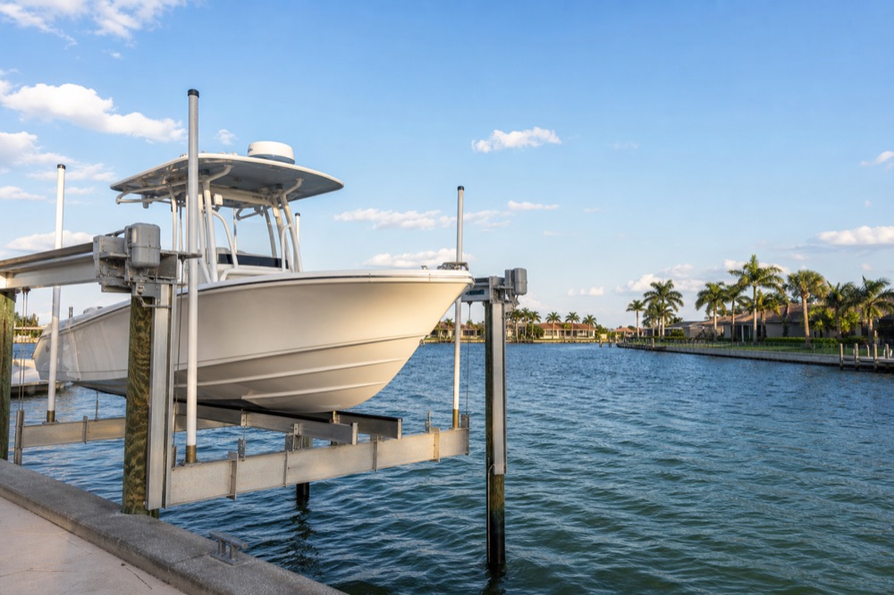A center console raised on an aluminum boat lift above a wide Southwest Florida canal with homes across the water